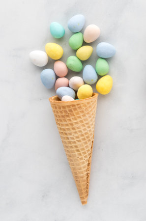 Single waffle cone filled with pastel coloured candy coated chocolates.