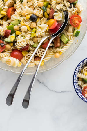 Above view of a pasta salad with long metal salad servers. Copy space below.の写真素材
