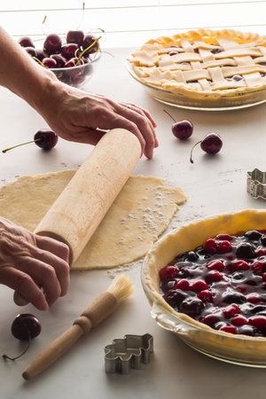 Hands using a rolling pin to roll out a pie shell to prepare a cherry pie.の写真素材