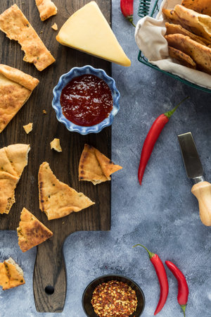 A board topped with a bowl of hot pepper jelly and seasoned cracker bread.