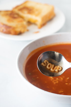 A bowl of alphabet tomato soup with the word soup spelled out in the spoon.の写真素材