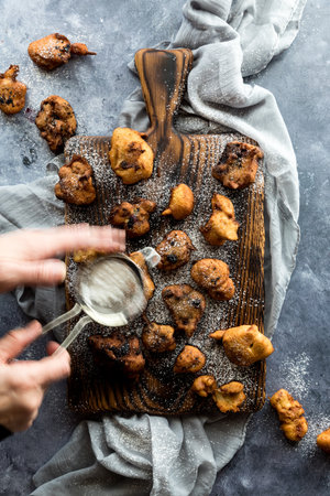 Blurry hands to depict motion of sprinkling powdered sugar on homemade fritters.の写真素材