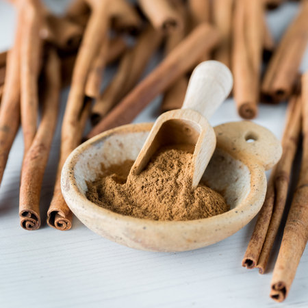 A small bowl of cinnamon powder with cinnamon sticks scattered in behind.
