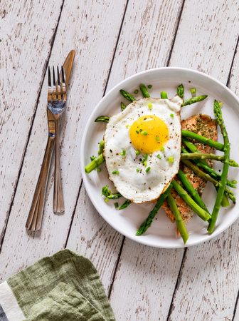 A serving of roasted salmon with sauteed asparagus and a fried egg on top.の写真素材