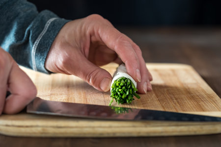a bundle of chives in a roll ready for slicing, on a wooden cutting board.の写真素材