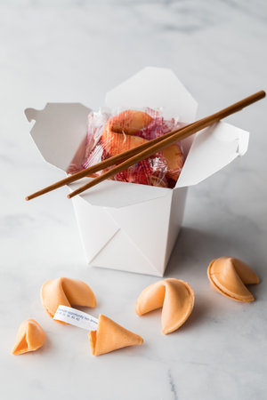 A takeout food container filled with fortune cookies with cookies in front.の写真素材
