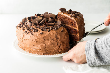 Hands removing a slice from a triple layered homemade chocolate cake.