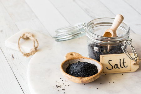 A jar and bowl filled with black Hawaiian rock salt on a marble slab.の写真素材