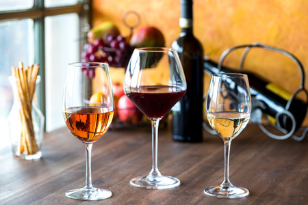 Glasses of rose, red and white wine on a wooden table.