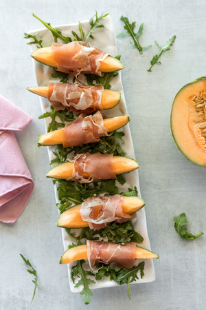 Top down view of cantaloupe wedges wrapped in prosciutto deli meat.の写真素材