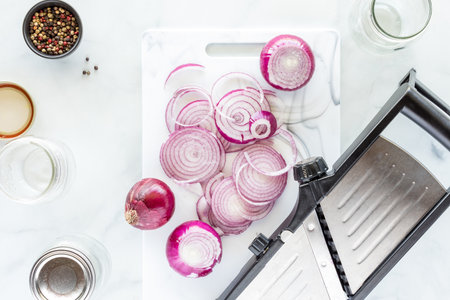 Sliced red onions with a mandolin beside, preparing for preservation.の写真素材