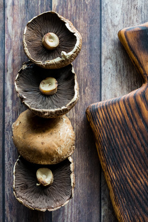 Fresh portobello mushrooms beside a wooden cutting board.の写真素材