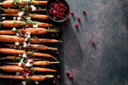 Roasted carrots garnished with pomegranate arils and copy space to the right.の写真素材