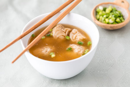 A bowl of wonton soup with slices of green onion, ready for eating.の写真素材