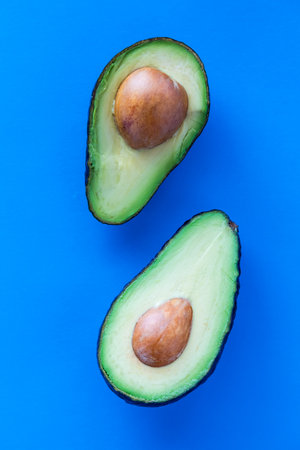 Cut avocados with the seed in the middle, against a bright blue backgroundの写真素材