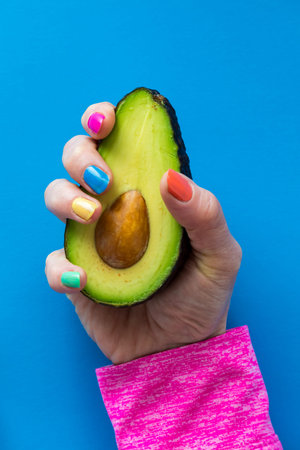 A hand with colourful nail polish holding a cut ripe avocado.の写真素材