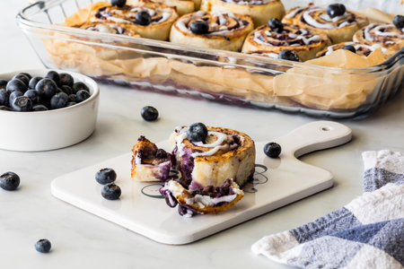 A torn fresh baked blueberry cinnamon roll with a tray of baked rolls in behind.の写真素材