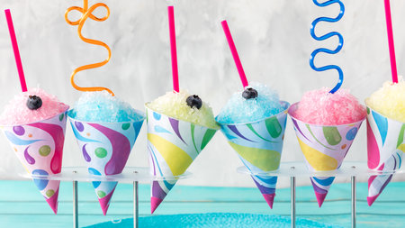 A row of flavoured snow cones with silly straws against a light background.の写真素材