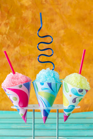Colourful snow cones in a stand against an orange background.の写真素材