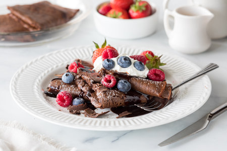 A plate of homemade chocolate crepes topped with whip cream and berries.の写真素材