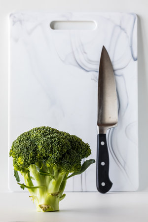 A standing broccoli stalk with a knife and cutting board in behind.の写真素材