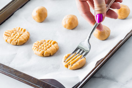 A hand pressing a fork into raw peanut butter cookies to make cross hatches.の写真素材