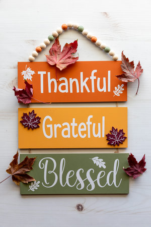 A wooden wall hanging with Thanksgiving themed words and leaves all around.