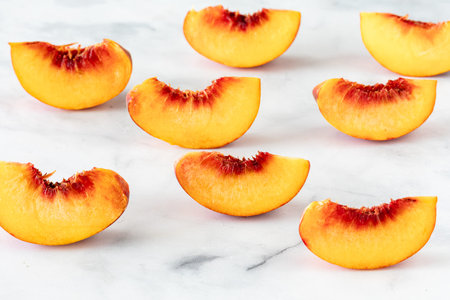 Slices of fresh free stone peaches on a white marble surface.の写真素材
