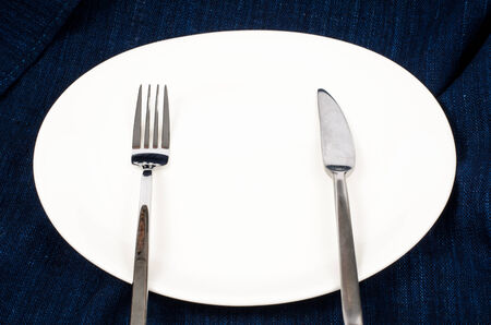 White plate with fork and knife on deep blue fabricの写真素材