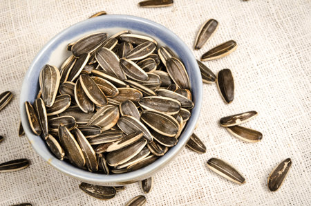 Image of sunflower seeds in ceramic bowl on white fabricの写真素材