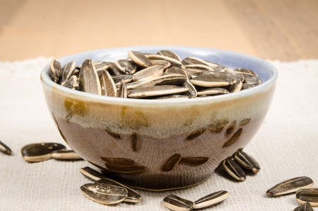 Image of sunflower seeds in ceramic bowl on white fabricの写真素材