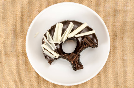 Chocolate donut with bite taken out in white dish on brown sack backgroundの写真素材