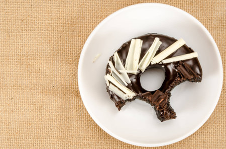 Chocolate donut with bite taken out in white dish on brown sack backgroundの写真素材