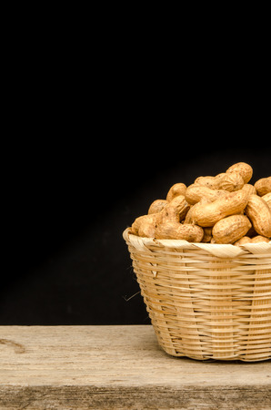 Peanuts in bamboo bucket on black backgroundの写真素材