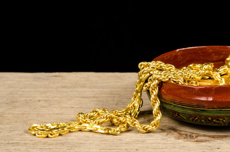 Gold neck lace in wood bowl on old wood with black backgroundの写真素材