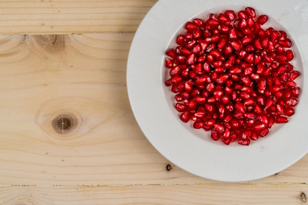 Red pomegranate seeds in white plate on wooden desk