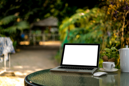 Mock up Blank screen of Laptop with a cup of coffee on glass table with green blurred backgroundの写真素材