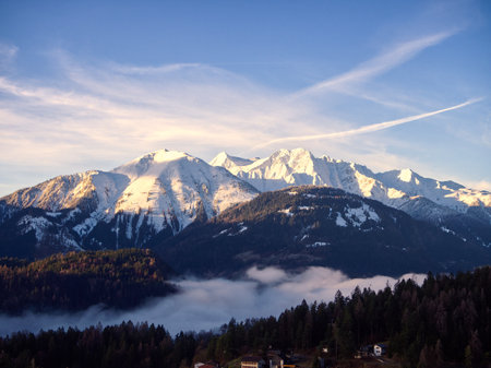 Alpine landscape snowcapped mountain view with low clouds at dawn in Laax, Switzerland. First rays of sunshine on the horizon. Calm mood.の写真素材