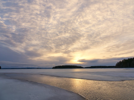Finnish frozen lake with reflections at sunset under dramatic sky.の写真素材