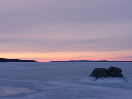 Frozen lake at sunset with a rock in the front in cracked iceの写真素材