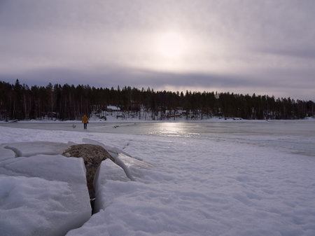 Frozen lake with a rock in the front with cracked ice and a person walkingの写真素材