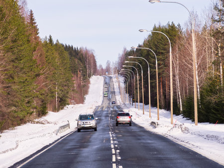 Asphalt highway with cars through the forest in a sunny winter day. Vanishing point.の写真素材