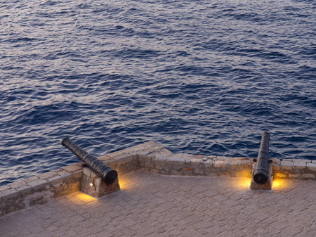 Hydra cobblestone fortified cannons and sea high angle view at blue hour. Saronic Gulf, Greece