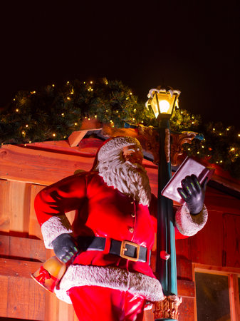 Santa Claus statue reading a book under Christmas lights at night view from belowの写真素材