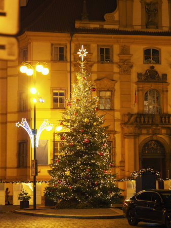 Illuminated Christmas tree in front of ornate building, with street lamps and decorative lights in Pragueの写真素材