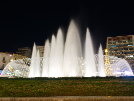 Night view of spectacular water fountain with illuminated jets and Christmas tree in urban plaza. Omonoia square. Athensの写真素材