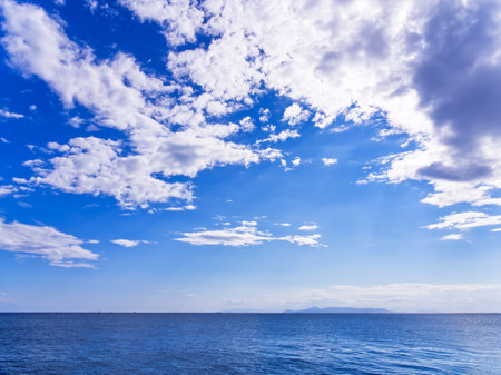 Vibrant blue sky with scattered white clouds over calm ocean waters on a clear dayの写真素材