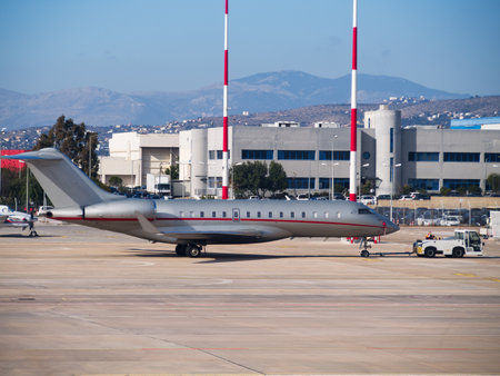 Luxury private jet parked on tarmac with airport buildings and mountains in backgroundの写真素材