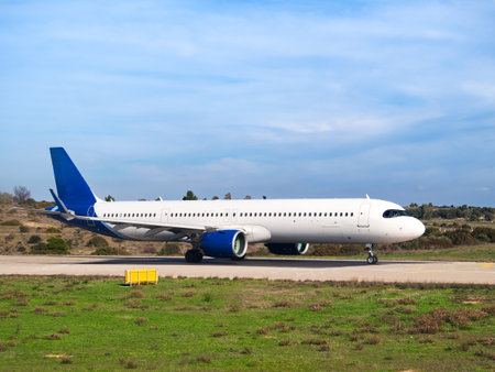 White and blue passenger aircraft on runway with grassy field and blue sky in backgroundの写真素材