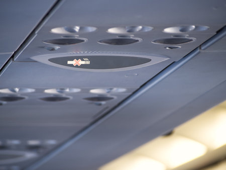Close-up of airplane ceiling panel showing air vents and illuminated no smoking signの写真素材